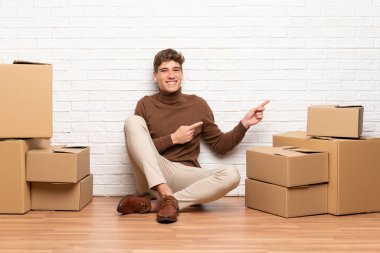 Yakışıklı genç adam yan parmak işaret kutuları arasında yeni bir evde hareket