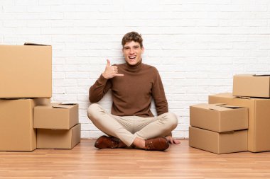 Yakışıklı genç adam telefon jest yapma kutuları arasında yeni evde hareket
