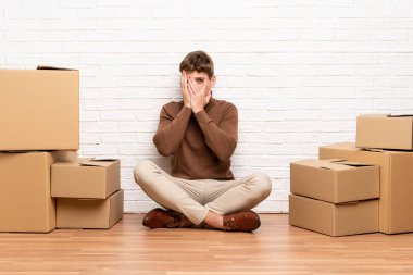 Yakışıklı genç adam gözleri kaplayan kutular arasında yeni bir evde hareket ve parmaklardan bakarak