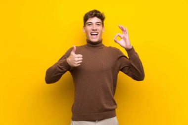 Izole sarı arka plan üzerinde yakışıklı genç adam ok işareti ve başparmak yukarı jest gösteren