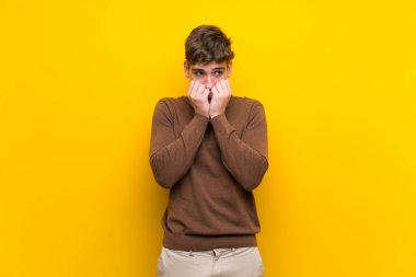 Izole sarı arka plan sinirli üzerinde Yakışıklı genç adam ve ağıza ellerini koyarak korkmuş