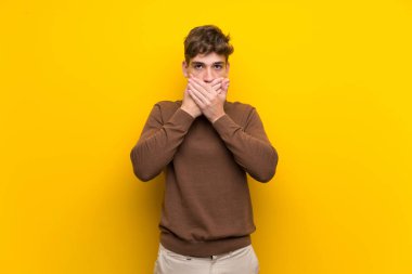 Elleri ile ağız kapsayan izole sarı arka plan üzerinde Yakışıklı genç adam