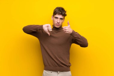 Izole sarı arka plan üzerinde yakışıklı genç adam iyi-kötü işareti yapma. Evet ya da değil arasında kararsız