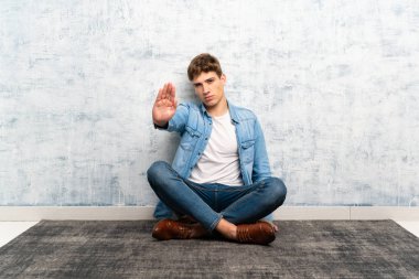 Yakışıklı genç adam eliyle stop jesti yaparak yerde oturuyor