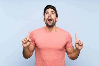 Izole mavi arka plan üzerinde pembe gömlek yakışıklı genç adam şaşırttı ve işaret