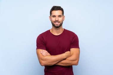 İzole edilmiş mavi arka planda yakışıklı bir adam kollarını ön tarafta çapraz tutuyor.
