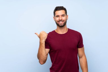 Soyutlanmış mavi arkaplan üzerinde yakışıklı bir adam bir ürün sunmak için kenarı işaret ediyor