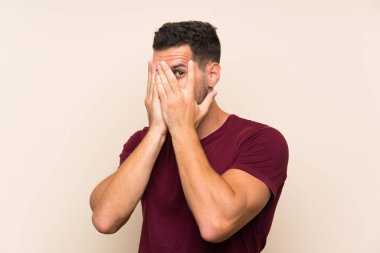 Gözleri kaplayan ve parmaklardan bakan izole arka plan üzerinde Yakışıklı adam