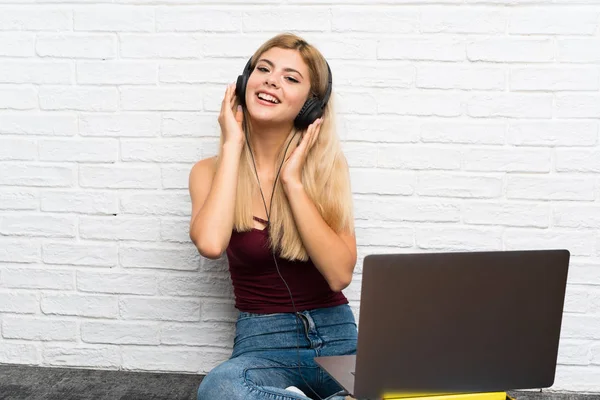 Chica adolescente sentada en el suelo con su portátil escuchando música —  Fotos de Stock