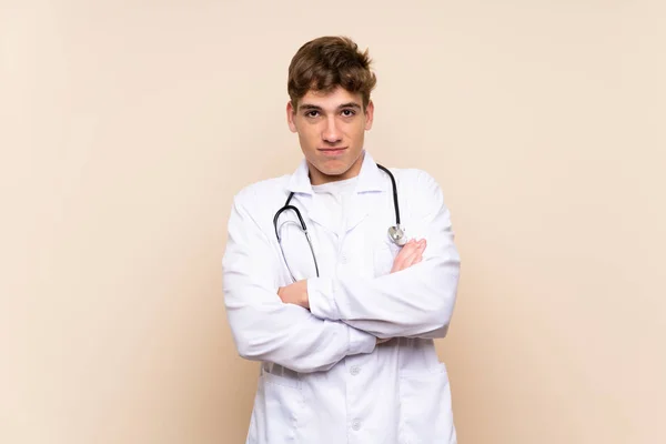 肩を持ち上げながら疑いのジェスチャーを作る孤立した壁の上のハンサムな医師の若者 — ストック写真