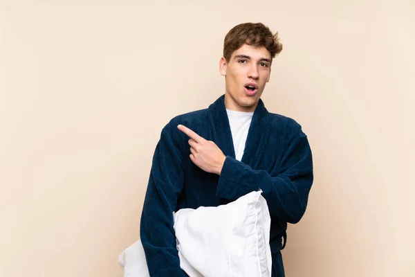 Handsome young man in pajamas over isolated wall surprised and pointing side