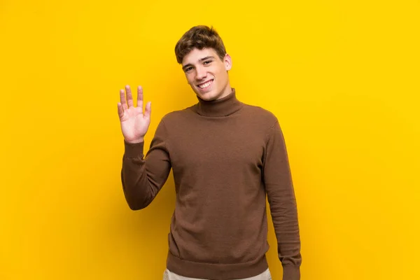 Przystojny Młody Człowiek Białym Tle Żółto Tło Pozdrawiając Ręką Szczęśliwym — Zdjęcie stockowe