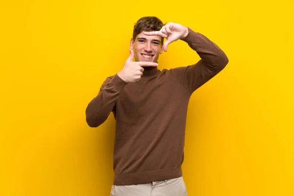 Handsome young man over isolated yellow background focusing face. Framing symbol