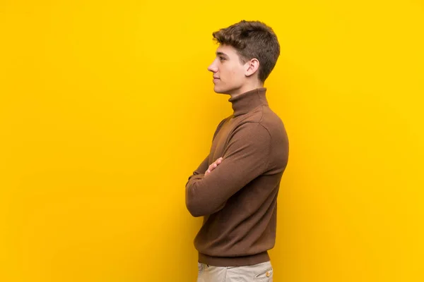 Handsome young man over isolated yellow background in lateral position