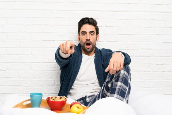 Man in bed with dressing gown and having breakfast surprised and pointing front