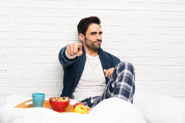 Man in bed with dressing gown and having breakfast points finger at you with a confident expression