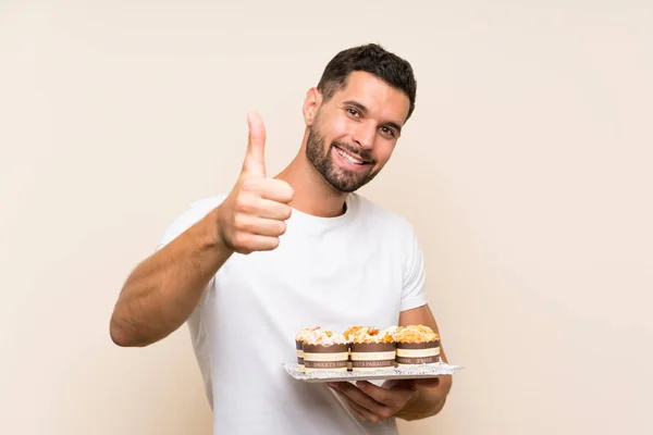 Handsome man holding muffin cake over isolated background with thumbs up because something good has happened