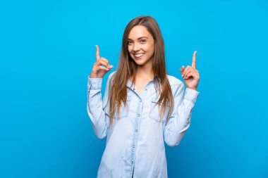 İzole edilmiş mavi arka planı olan genç bir kadın harika bir fikre işaret ediyor.