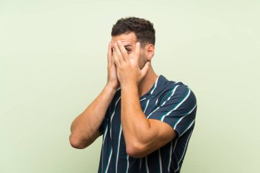 Gözleri kaplayan ve parmaklardan bakan izole arka plan üzerinde Yakışıklı adam