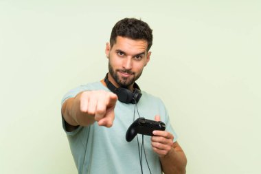 Genç yakışıklı adam kendinden emin bir ifade ile size izole yeşil duvar noktaları parmak üzerinde bir video oyunu denetleyicisi ile oynuyor