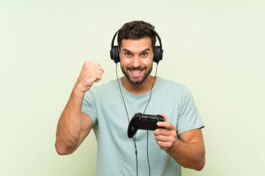 İzole yeşil duvar üzerinde bir video oyunu denetleyicisi ile oynayan genç yakışıklı adam