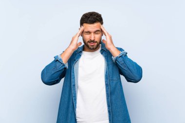 Başı ağrıyan, soyutlanmış mavi arka planı olan yakışıklı bir adam.