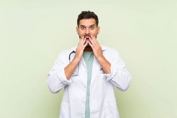 Young doctor man over isolated green wall with surprise facial expression