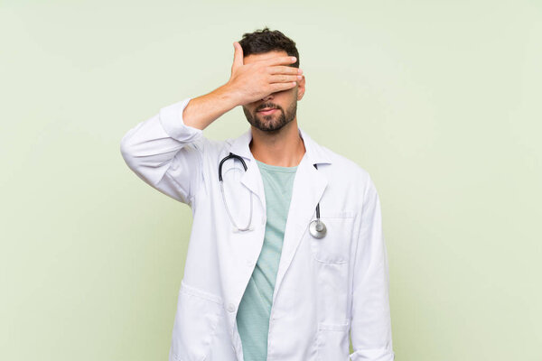 Young doctor man over isolated green wall covering eyes by hands