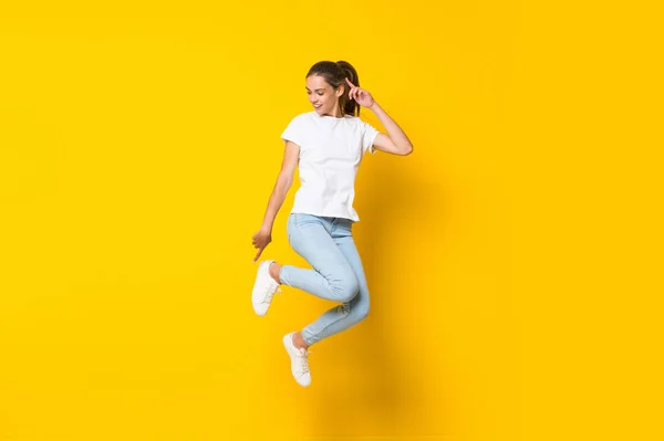 Mujer joven saltando sobre la pared amarilla aislada —  Fotos de Stock