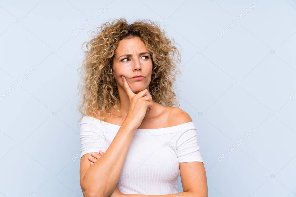 Young blonde woman with curly hair over isolated blue background thinking an idea