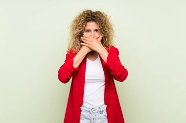 Elleri ile ağız kapsayan izole yeşil arka plan üzerinde kıvırcık saçlı genç sarışın kadın