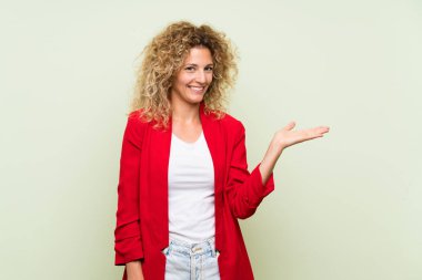 Bir reklam eklemek için avuç üzerinde copyspace hayali tutan izole yeşil arka plan üzerinde kıvırcık saçlı genç sarışın kadın