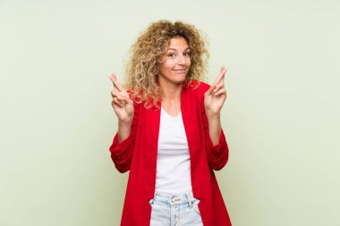 Parmakları geçiş ve en iyi dilek ile izole yeşil arka plan üzerinde kıvırcık saçlı genç sarışın kadın