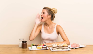 Ağzı tamamen açık bağıran bir masada farklı mini kek çok genç kadın