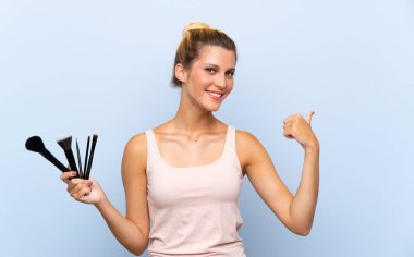 Genç sarışın kadın bir ürün sunmak için yan işaret makyaj fırçası çok tutan