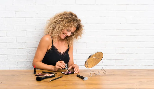 Mujer joven con mucho cepillo de maquillaje en una mesa — Foto de Stock