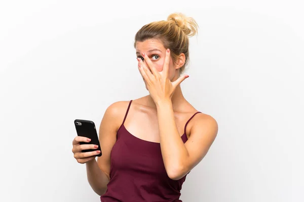 目を覆い 指を通して見ている携帯電話を使用して若いブロンドの女性 — ストック写真