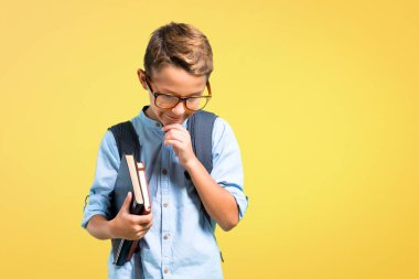 Sırt çantası ve gözlük ile Öğrenci çocuk ayakta ve sarı arka plan aşağı bakıyor