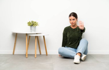 Genç kadın eliyle dur jesti yaparak yerde oturuyor