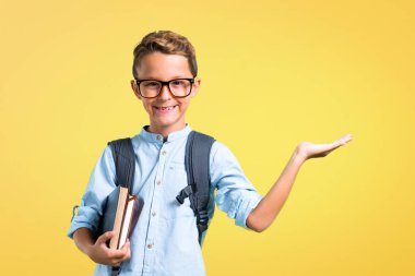 Sırt çantası ve gözlük sarı arka plan üzerinde avuç üzerinde hayali copyspace tutan öğrenci çocuk