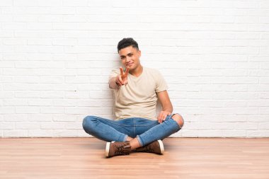 Yerde oturan genç adam gülümsüyor ve zafer işareti gösteriyor.