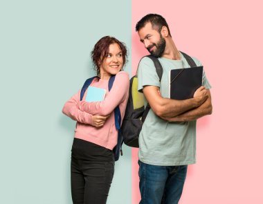 Sırt çantaları ve renkli duvarda bir gülümseme ile omuz üzerinden bakan kitap ile iki öğrenci