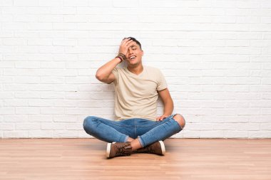 Genç adam yerde oturmuş gülüyor.