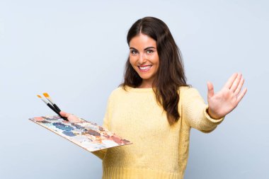 Izole mavi arka plan üzerinde genç sanatçı kadın mutlu ifade ile el ile selamlama