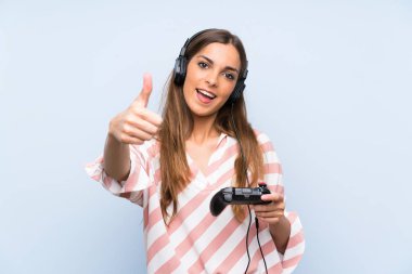 Genç kadın iyi bir şey oldu çünkü başparmak ile izole mavi duvar üzerinde bir video oyunu denetleyicisi ile oynuyor