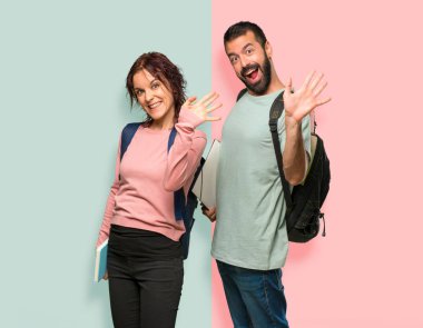 Renkli duvarda mutlu ifade ile el ile selamlayan sırt çantaları ve kitapları ile iki öğrenci