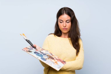 Üzgün ifade ile izole mavi arka plan üzerinde genç sanatçı kadın