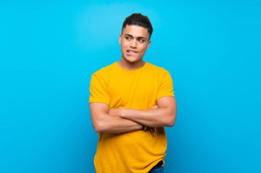 Karışık yüz ifadesi ile izole mavi arka plan üzerinde sarı gömlek li genç adam