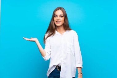 İzole edilmiş mavi arka plan üzerinde genç bir kadın bir ilan vermek için avucunun içinde hayali bir alan tutuyor.