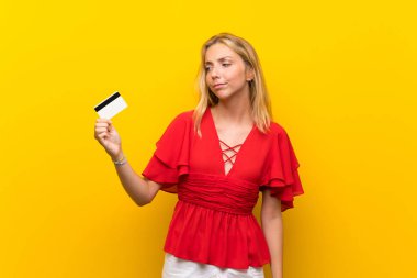 Bir kredi kartı tutan izole sarı arka plan üzerinde Sarışın genç kadın